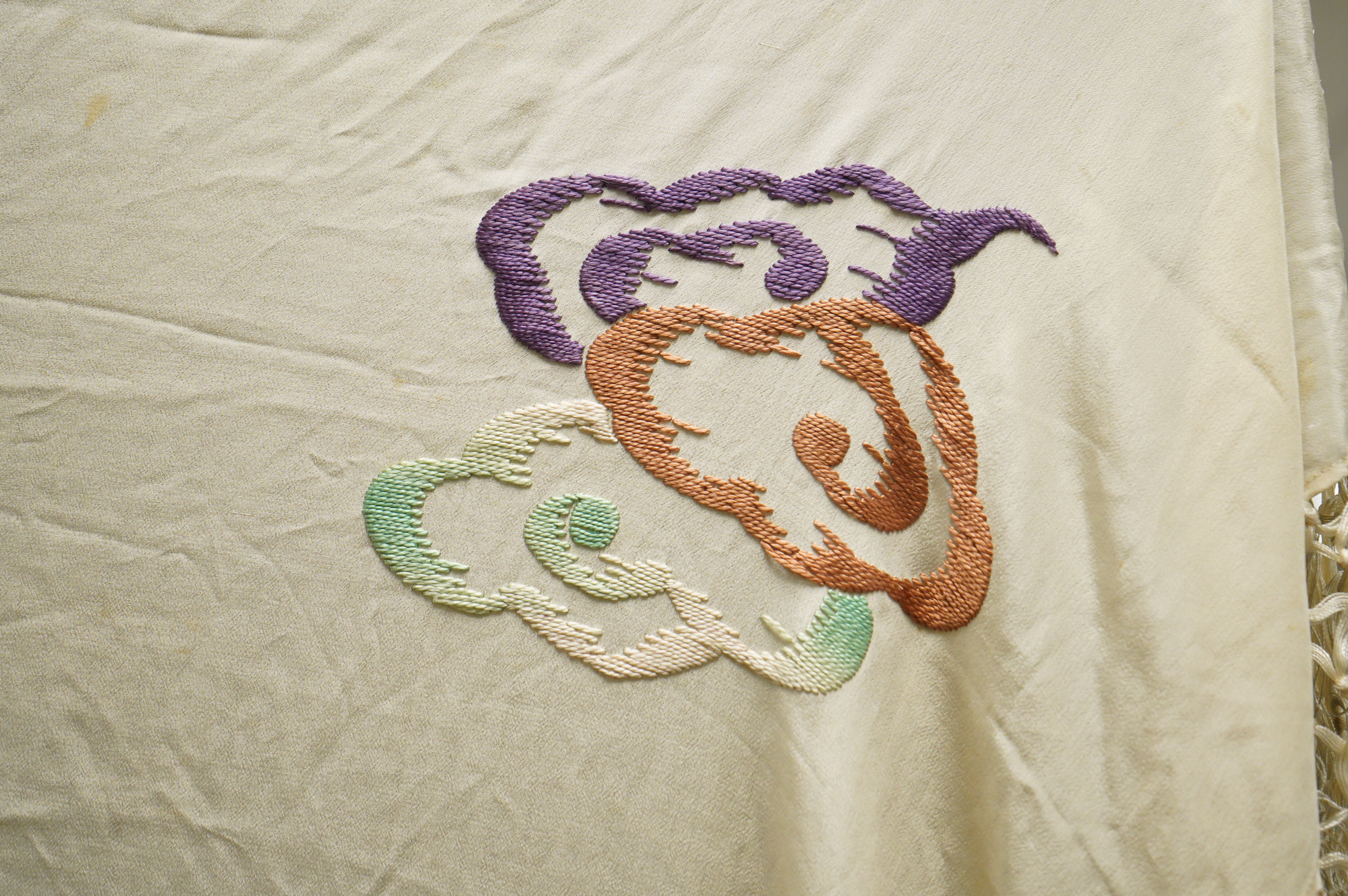 A unusual Chinese 1920’s-30’s cream silk fringed shawl, embroidered with a large central motif of a phoenix in flight, embroidered in bright multi coloured silks. 108cm x 100cm, Condition - there are some stains.